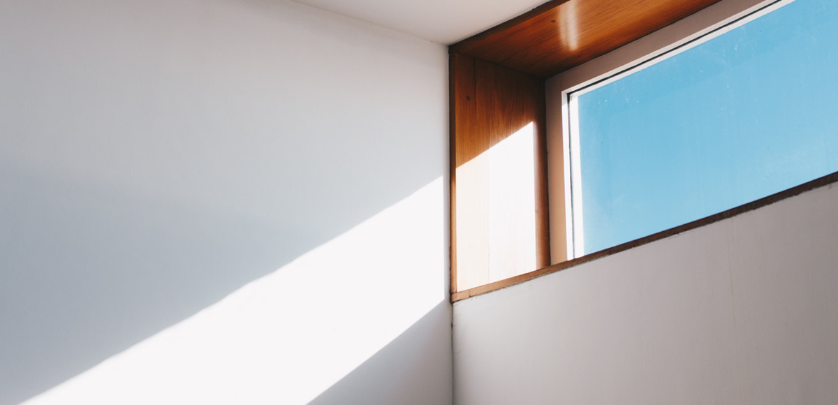 A high window with sunlight streaming through on a white wall
