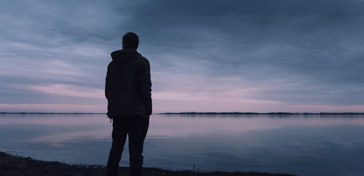 Silhouette of a man staring at the sunset across a lake