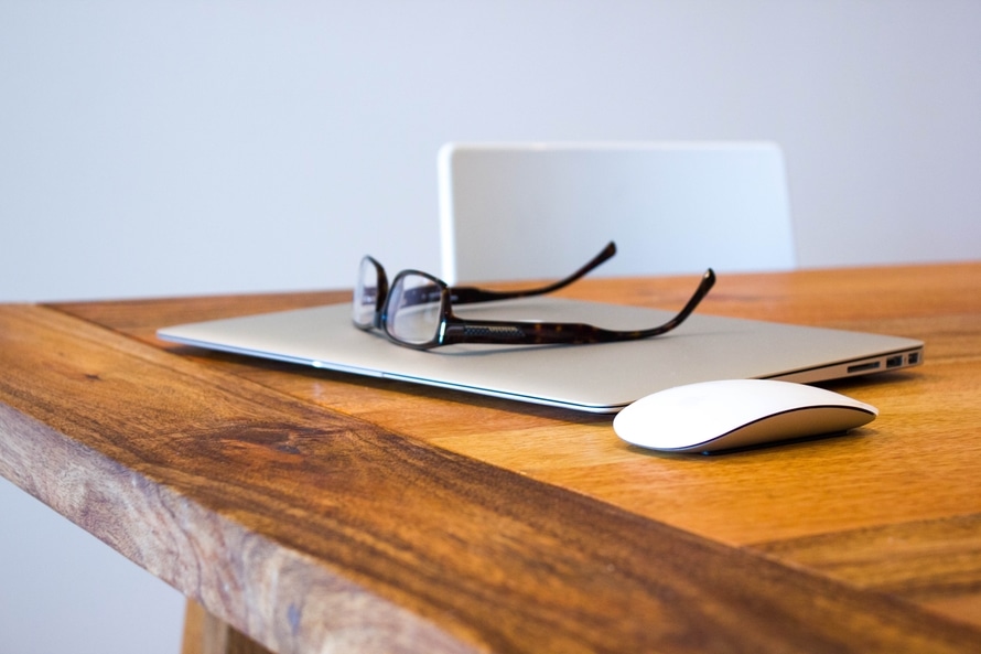 Glasses, laptop, and mouse sitting on a wooden desk