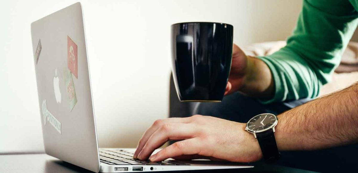 Man holding a coffee mug and typing on a mac laptop