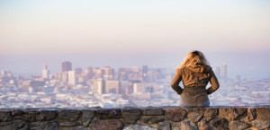 Woman sitting on a stone ledge overlooking a city in the distance