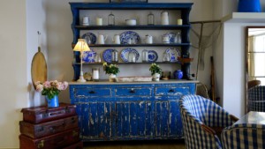 A distressed blue wooden hutch featuring rows of dishes and in need of refurbishing