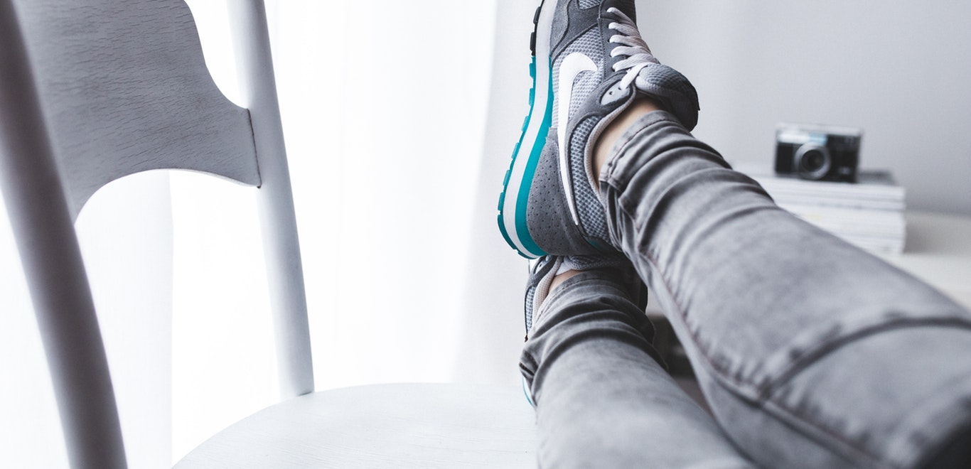 Legs up and crossed on chair, wearing grey jeans and grey Nike sneakers with camera in background