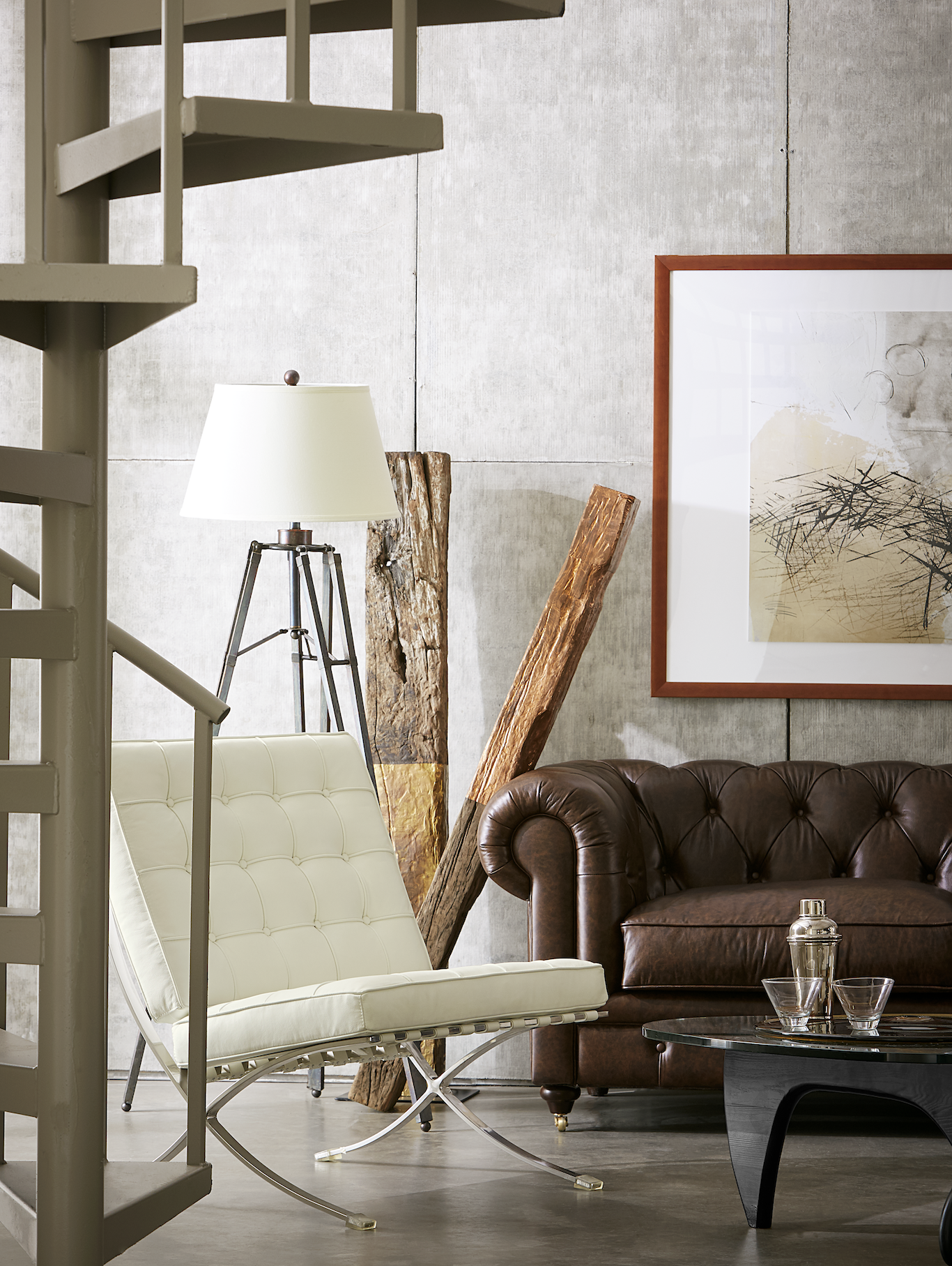 Brown sofa in a large room with cement walls, large white chair, and modern art decor