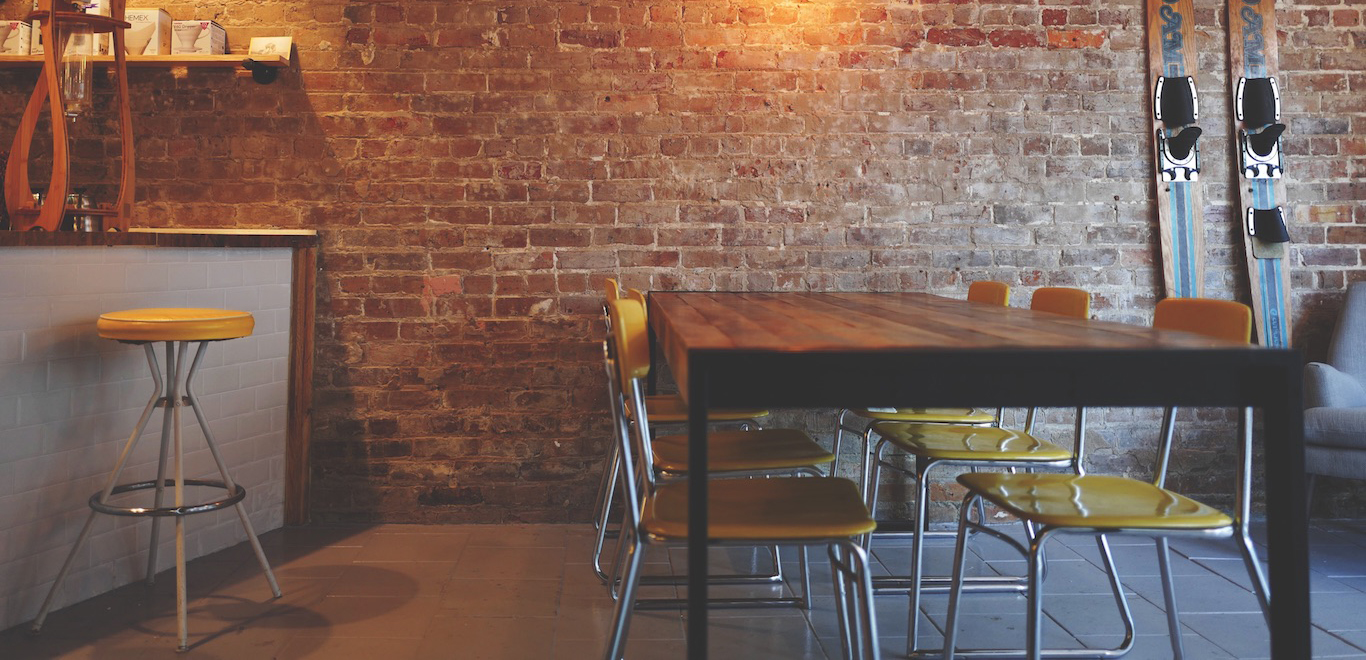 Dining table with yellow metal chairs, brick walls, and bar with a yellow metal barstool
