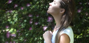 Woman with sunlight on her face surrounded by purple flowers and greenery