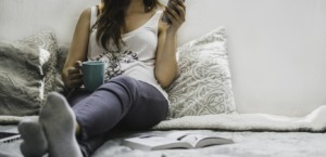 Woman against a white background holding a coffee mug and wearing gray pants