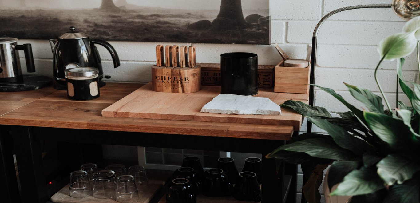 Wooden countertop with cutting board and cheese knives, against a white wall with framed artwork