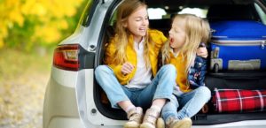 Little girls sitting in the trunk of a car next to packed suitcases