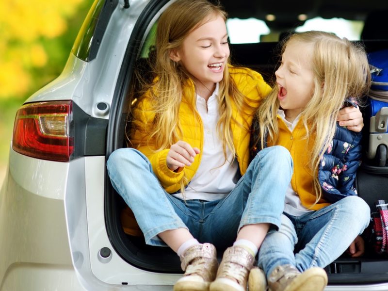 Little girls sitting in the trunk of a car next to packed suitcases