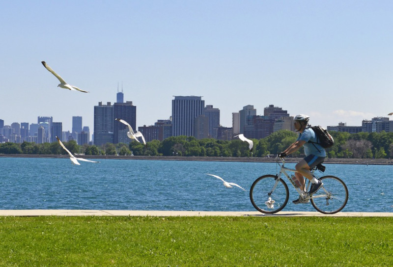 Cyclist with a backpack riding on a sidewalk along the lake with the Chicago skyline in the background