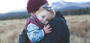 Toddler resting her head on her father's shoulder outdoors with mountains in the background