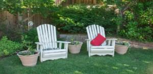 Two white wooden patio chairs sit on a lawn next to potted flowers