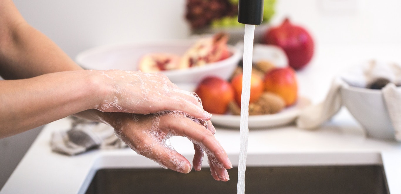 Soapy hands under a kitchen faucet with running water