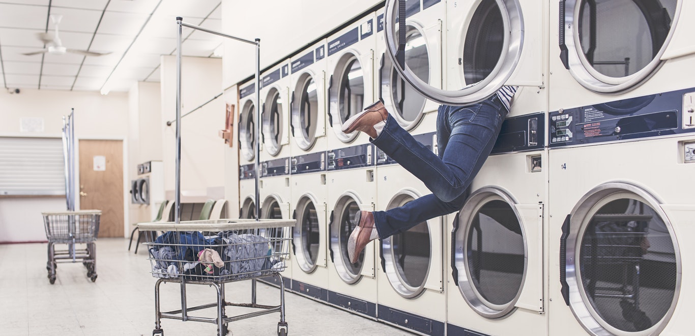 Person searching in the top dryer at a laundromat with legs dangling