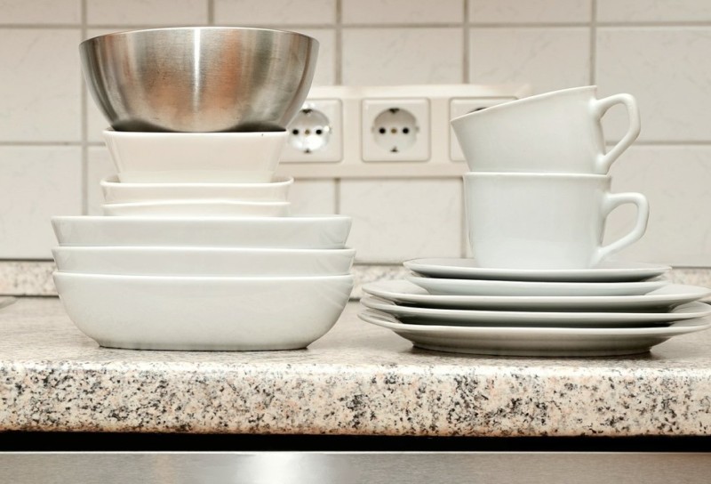White dishes, mugs, and an aluminum bowl sitting on a clean granite countertop.