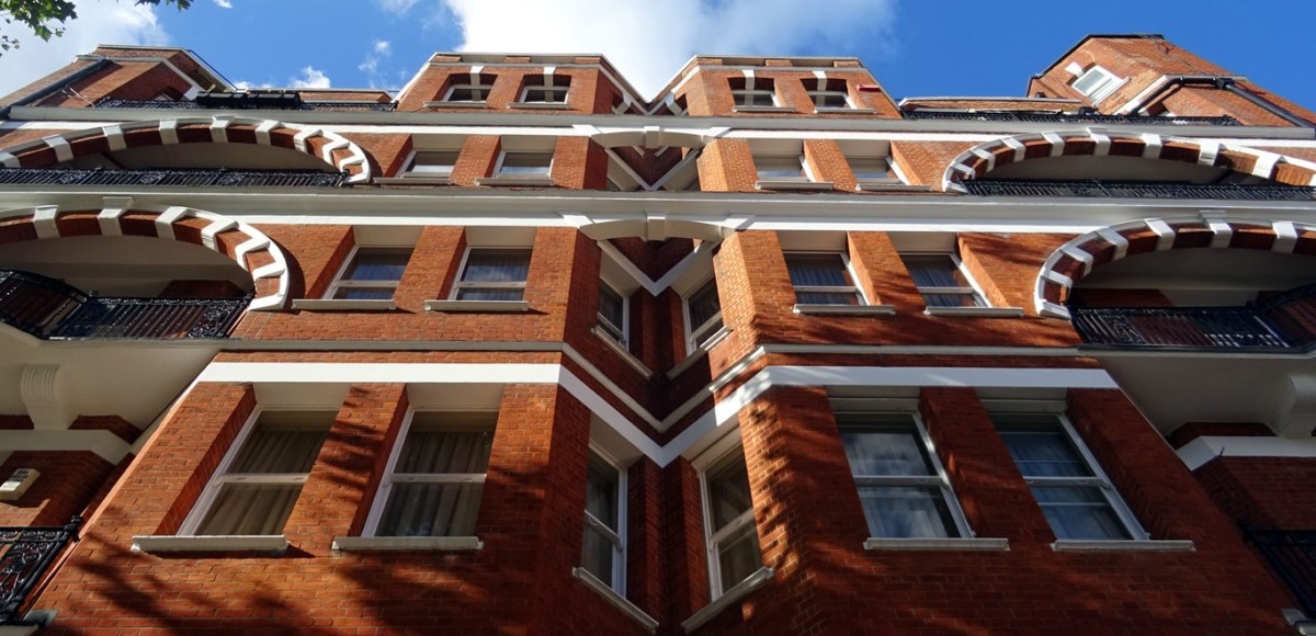 Dramatic upward view of red-brick apartment building with blue sky and white clouds in the background
