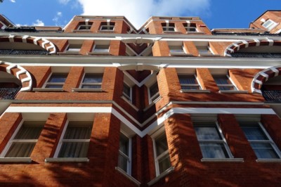 Dramatic upward view of red-brick apartment building with blue sky and white clouds in the background