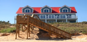 Beach home with red roof and wooden staircase leading to sandy beach