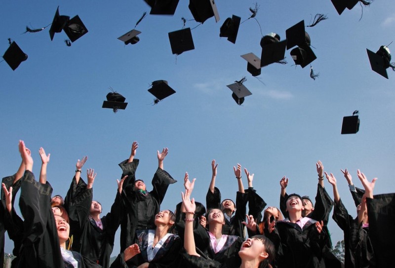 Smiling graduates in gowns throwing caps in the air against a blue sky