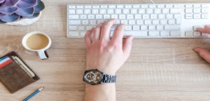 Man typing on keyboard with a cup of coffee, wallet, and pencil on his desk