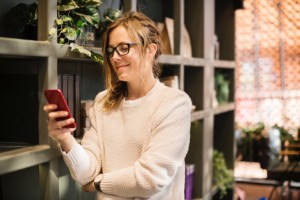 Woman looking at her phone with plants and books in the background