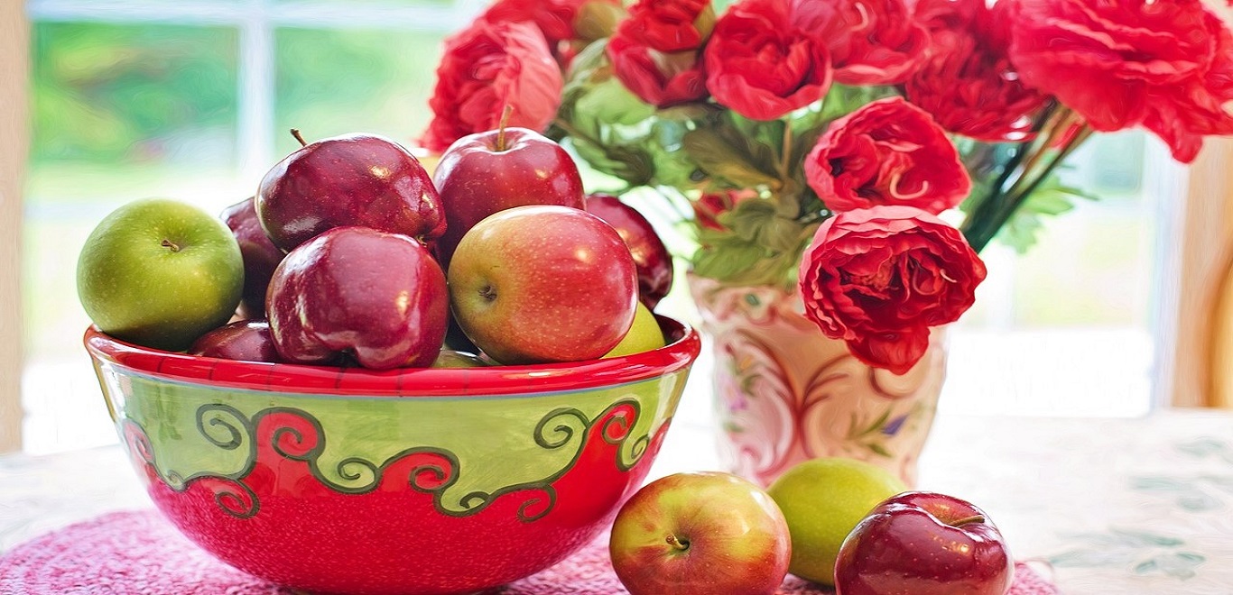 Fresh cut flowers in a pretty vase and a bowl of apples on a table