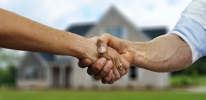 Close-up of handshake in front of single-family home