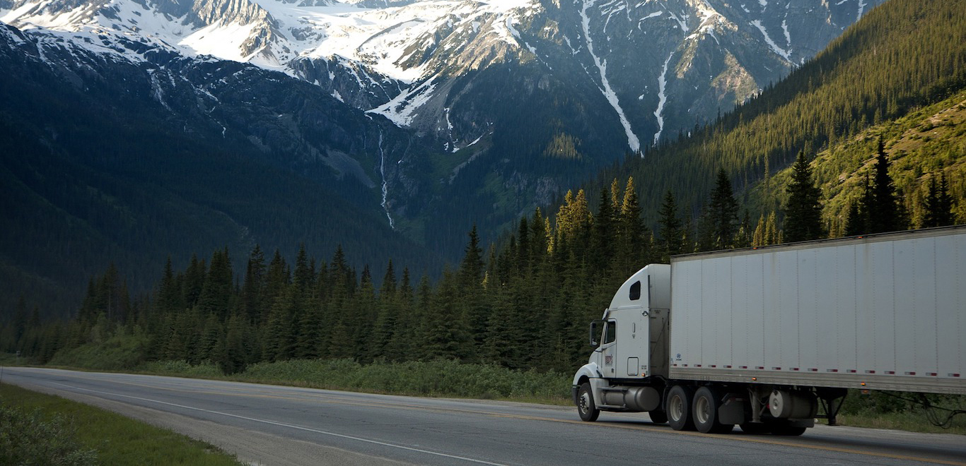 Large white moving van on a road with mountains and blue sky in the background