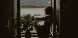 A woman sitting in shadows on a window ledge starting out the window