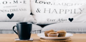 A mug, a plate of muffins, and pillows with positive messages