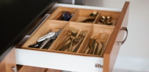 An open kitchen utensil drawer showing forks, knives, and spoons in a wooden organizer