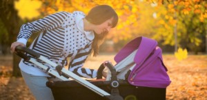 Woman tending to her baby in a stroller with fall foliage in the background