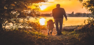 Father and son walking toward the water at sunset