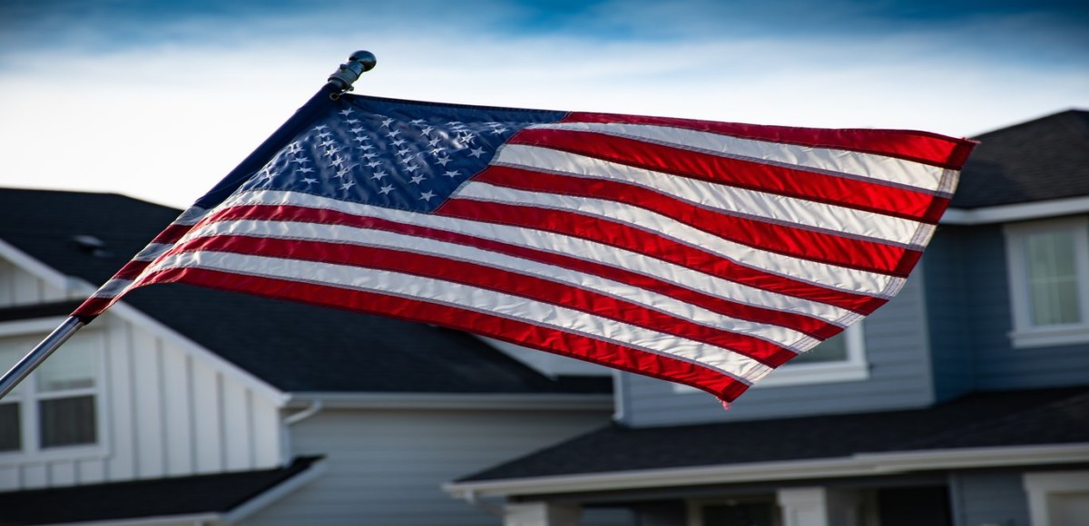 Close-up of an American flag waving in the wind with houses in the background