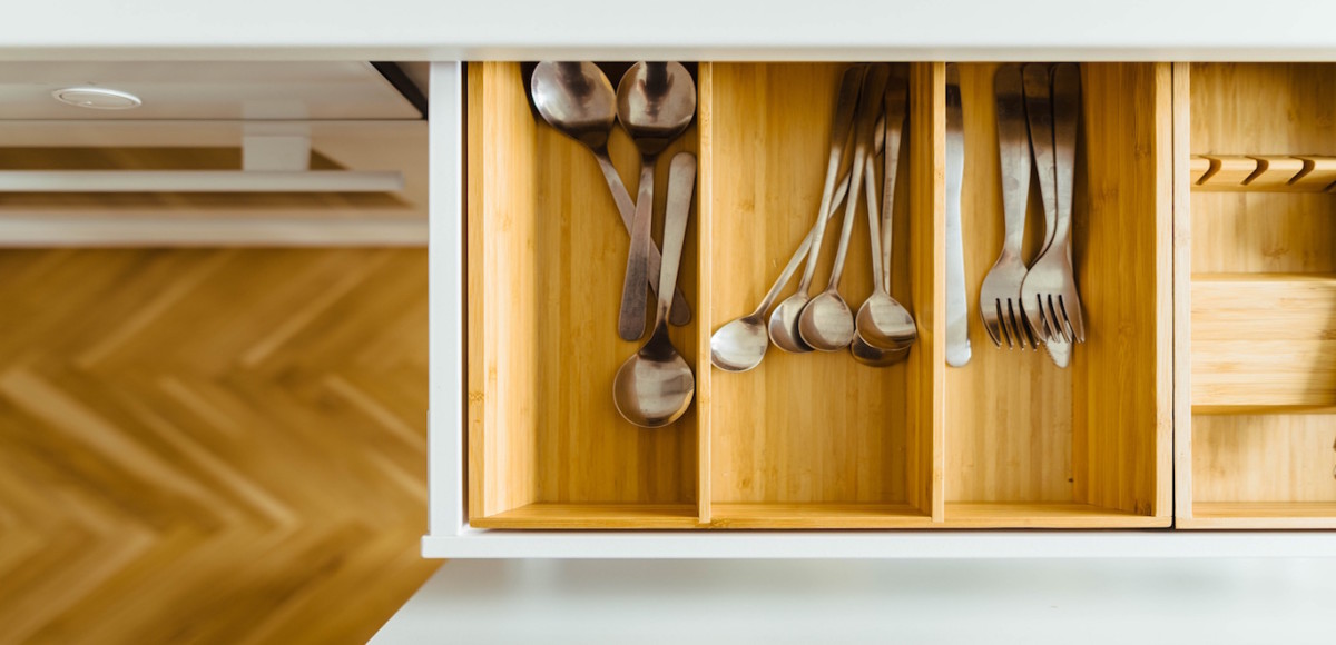An open drawer in a kitchen filled with utensils, spoons, forks in a wooden organizer