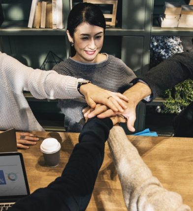 Group of office workers connecting hands around a wood table celebrating teamwork