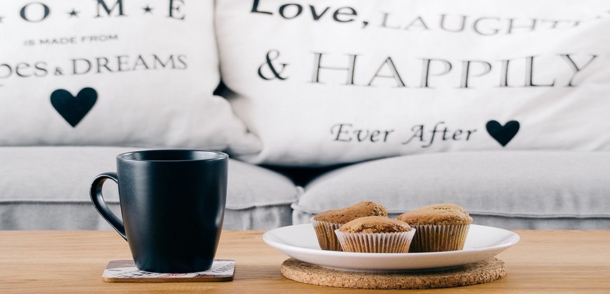 Three muffins and black coffee cup on a coffee table, white couch in background