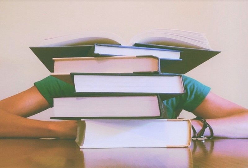 Young adult sitting at a table behind a stack of books