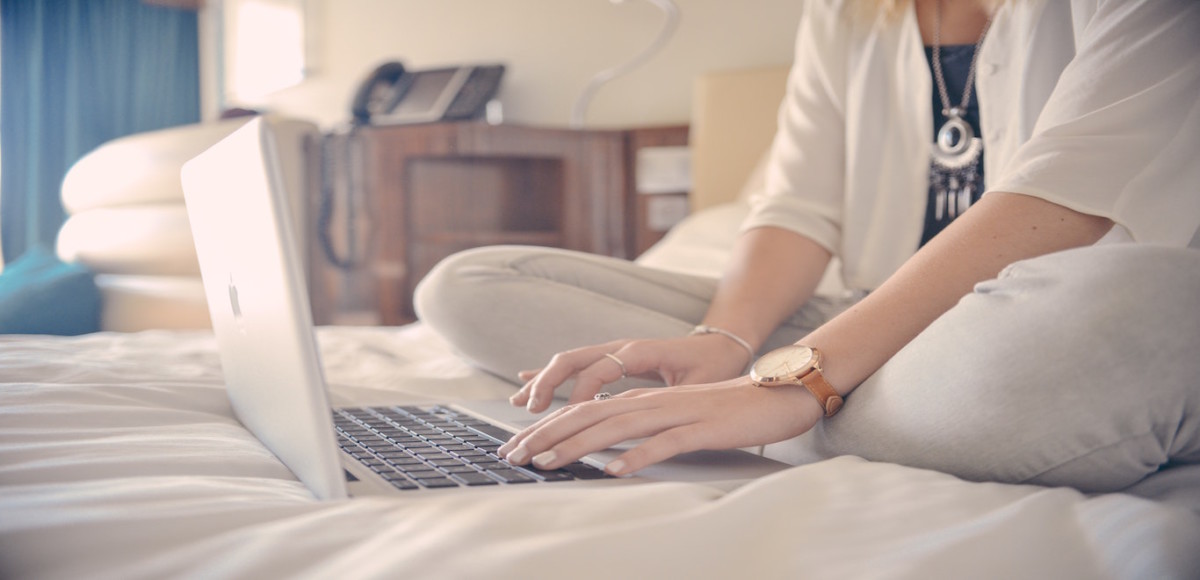 Woman typing on a laptop while sitting on a bed
