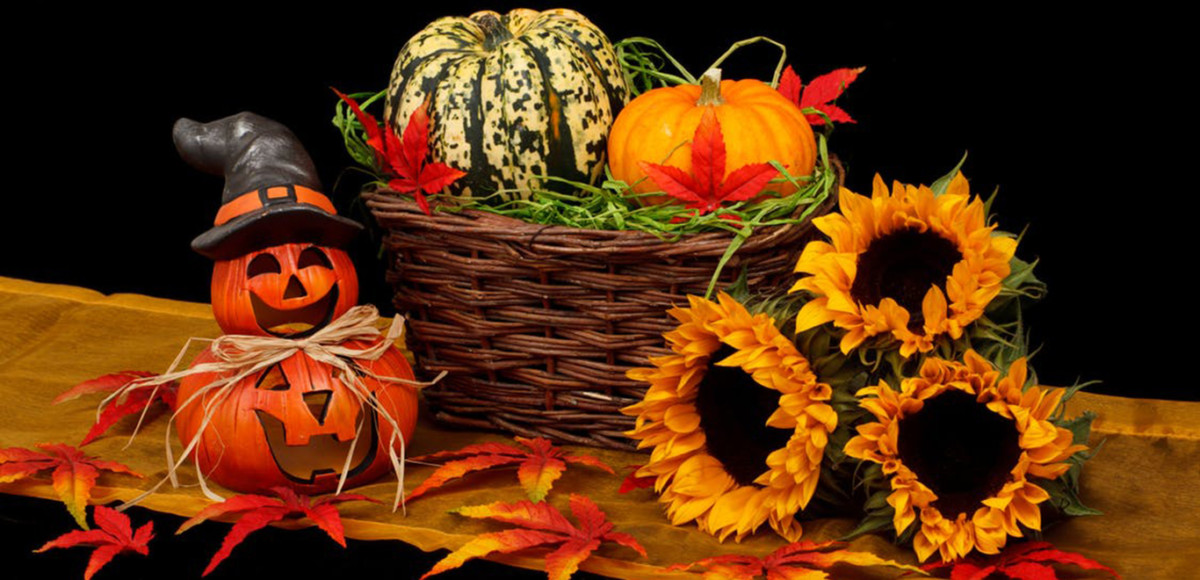 Gold and orange leaves, jack-o-lanterns, gourds, sunflowers, and a wicker basket on a table