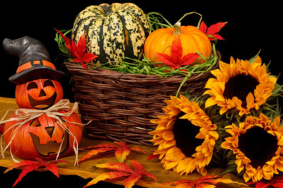 Gold and orange leaves, jack-o-lanterns, gourds, sunflowers, and a wicker basket on a table