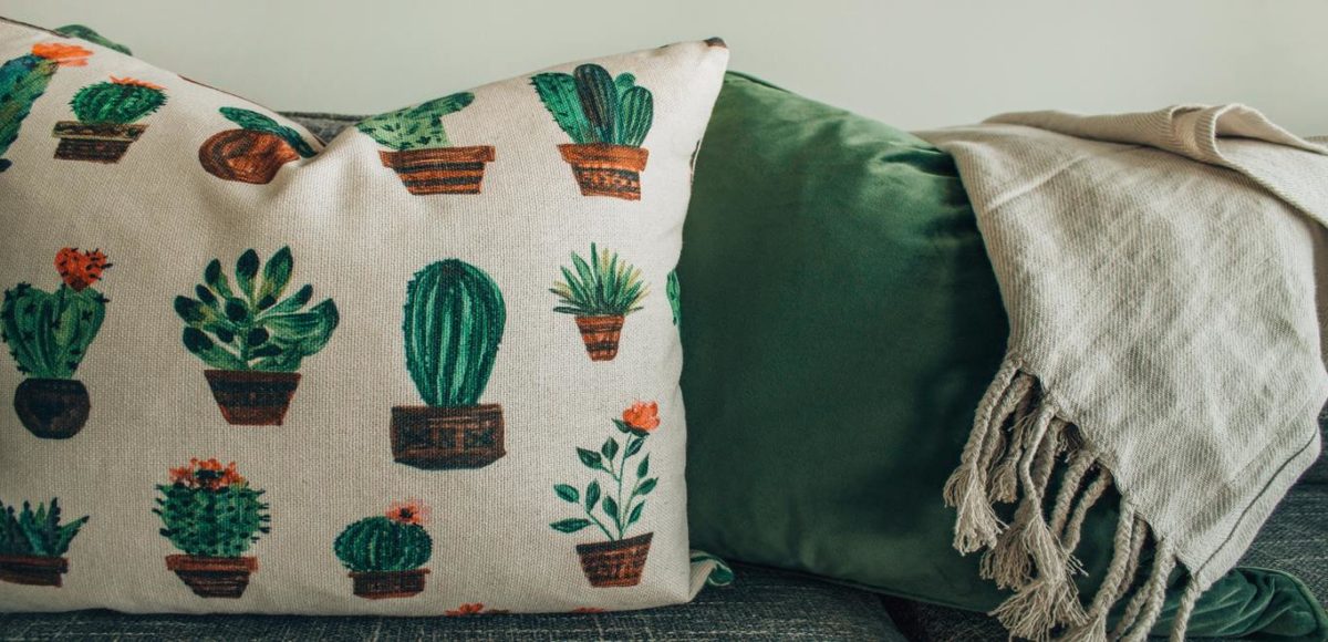 A throw pillow covered in cacti is situated next to a green throw pillow
