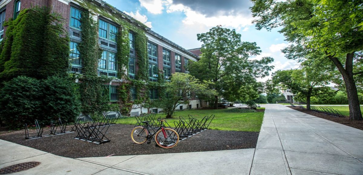 A bike is parked next to a walkway in front of a large, moss-covered campus building
