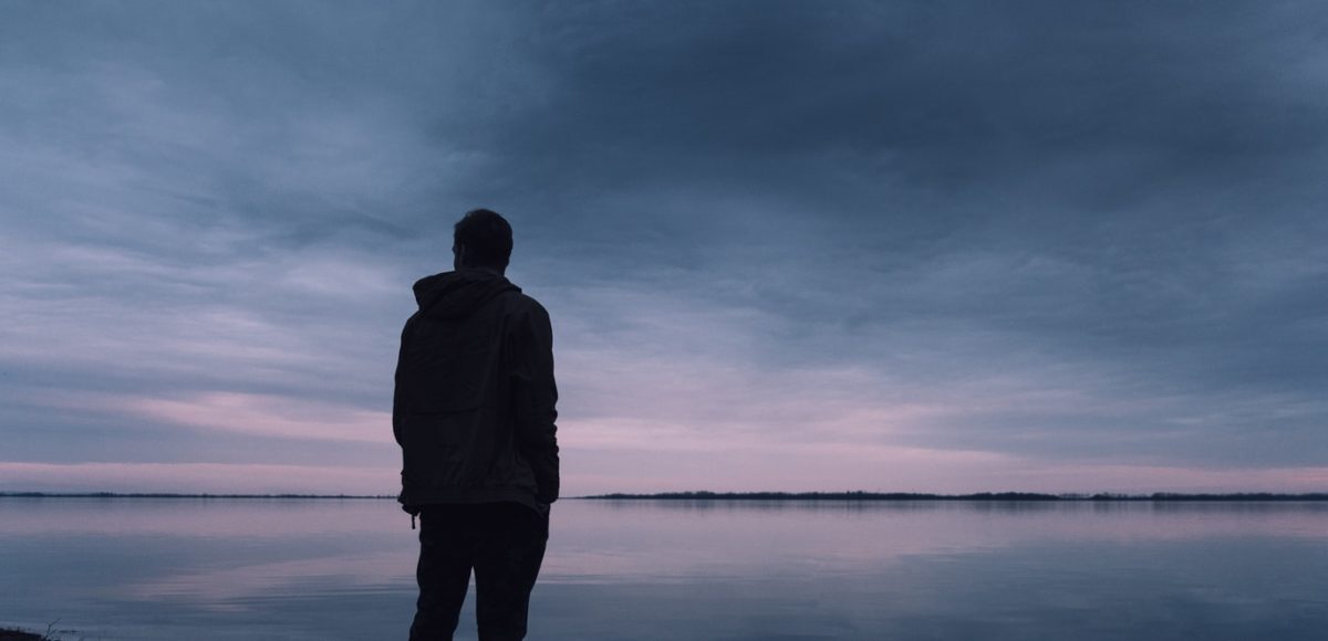 Man standing alone at the edge of the water at sunset