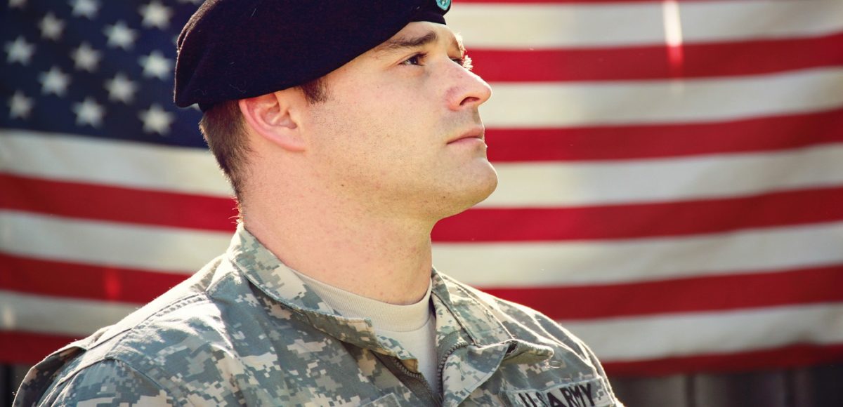 Male in a U.S. Army uniform standing in front of the American flag