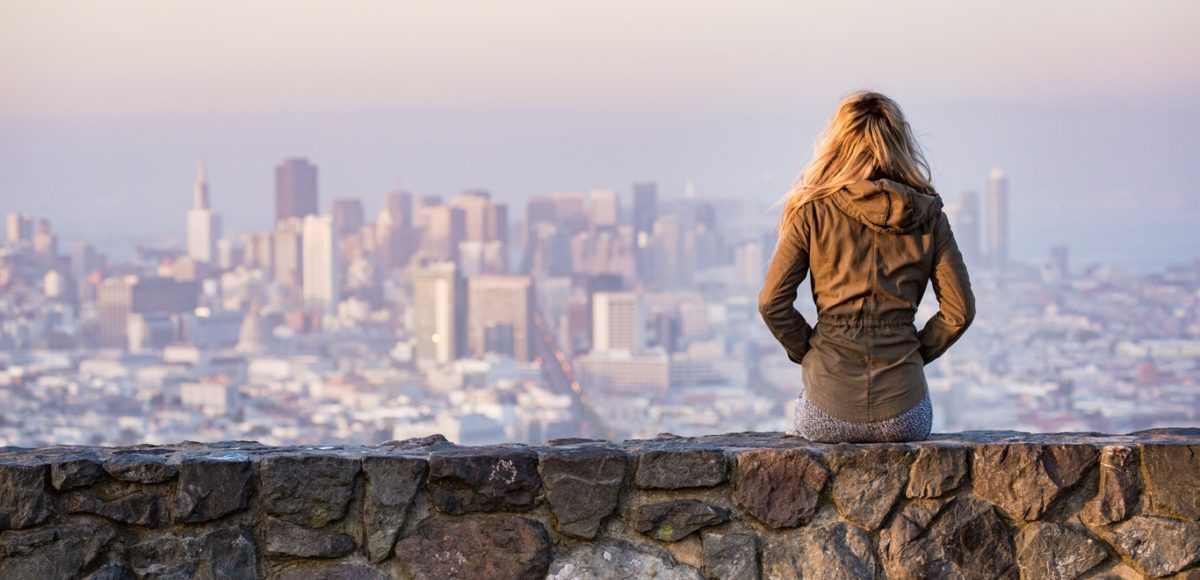 Young woman sitting on a stone wall overlooking a hazy urban city in the distance