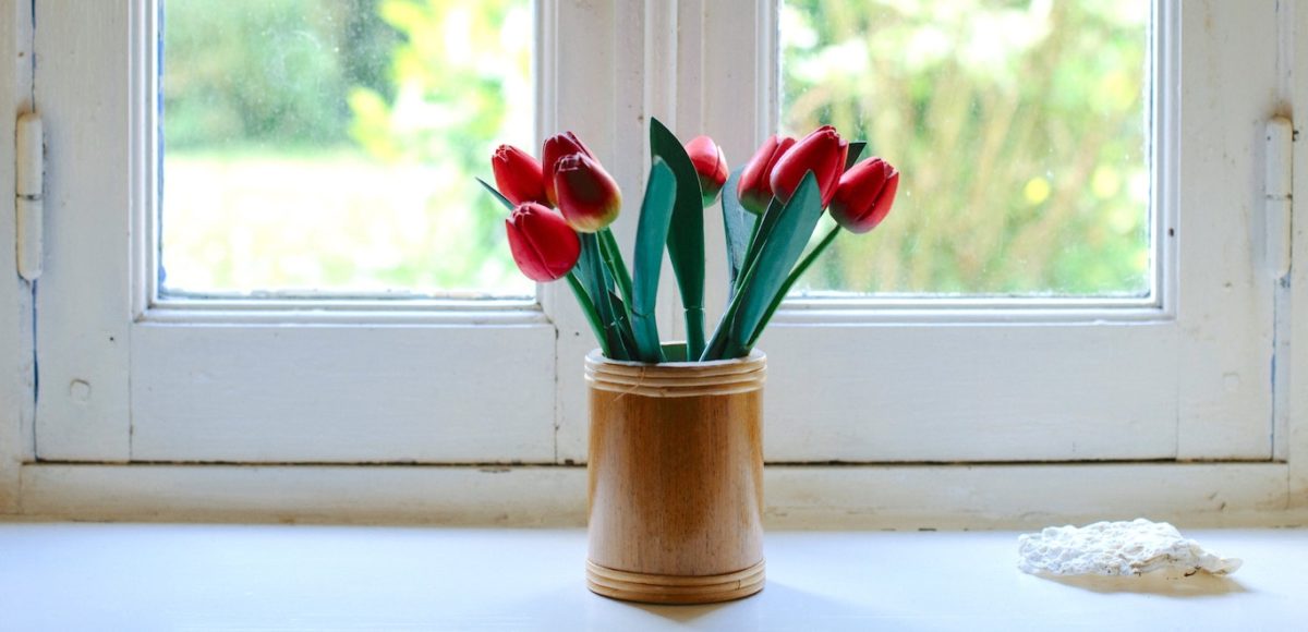 Wood vase filled with pink tulips sitting on a white, sunny windowsill