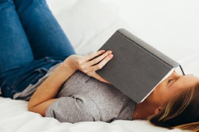 College girl taking a break while reading a book on her bed
