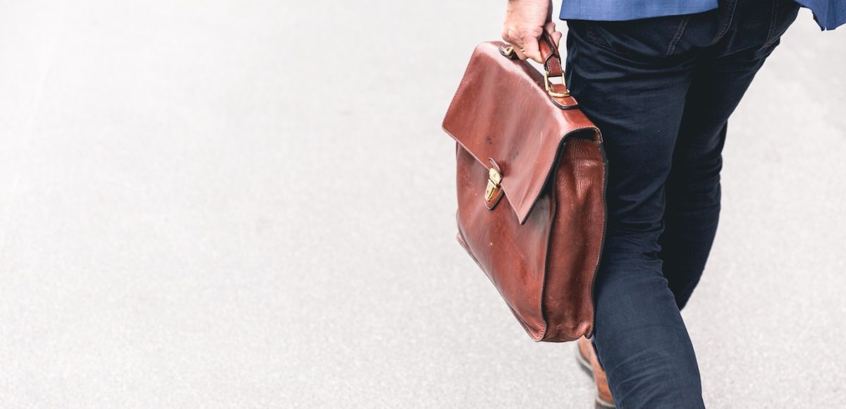 Businessman carrying a brown leather briefcase and walking along a sidewalk in daylight